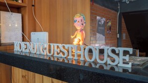 Una mesa de recepción con un cartel que dice "KOENJIGUESTHOUSE" y una pequeña figurita.