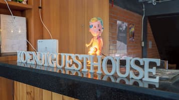 A reception desk with a sign that reads "KOENJIGUESTHOUSE" and a small figurine.