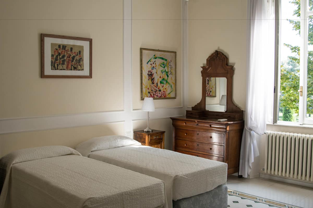 Ein Hotelzimmer mit zwei Betten, einem Schminktisch, einem Spiegel und zwei gerahmten Kunstwerken an der Wand.