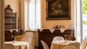 Un comedor con una araña, mesas con manteles blancos, sillas, un aparador de madera y un cuadro en la pared.