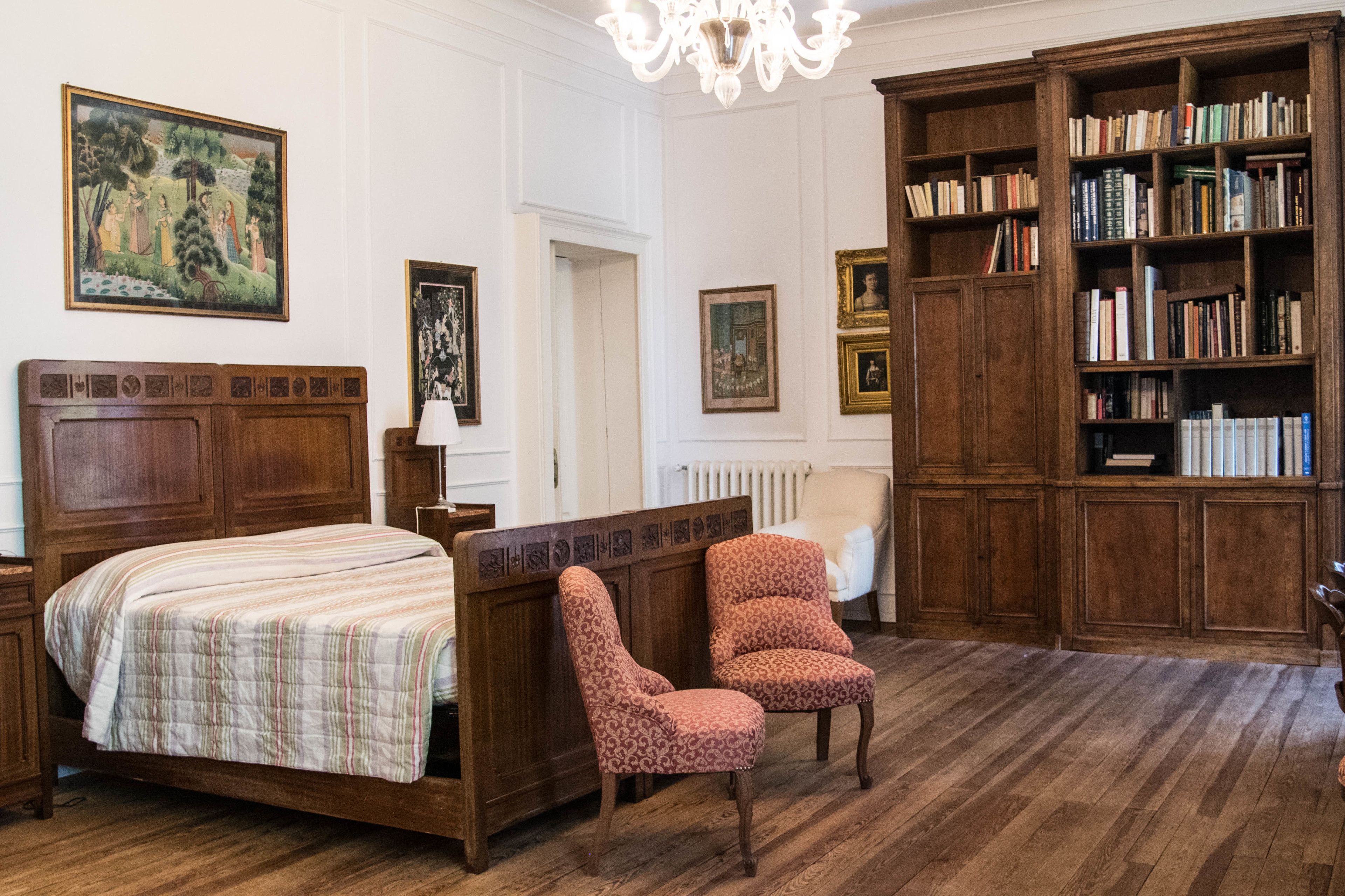 A room with a wooden bed, a chair, a bookshelf, and a chandelier.