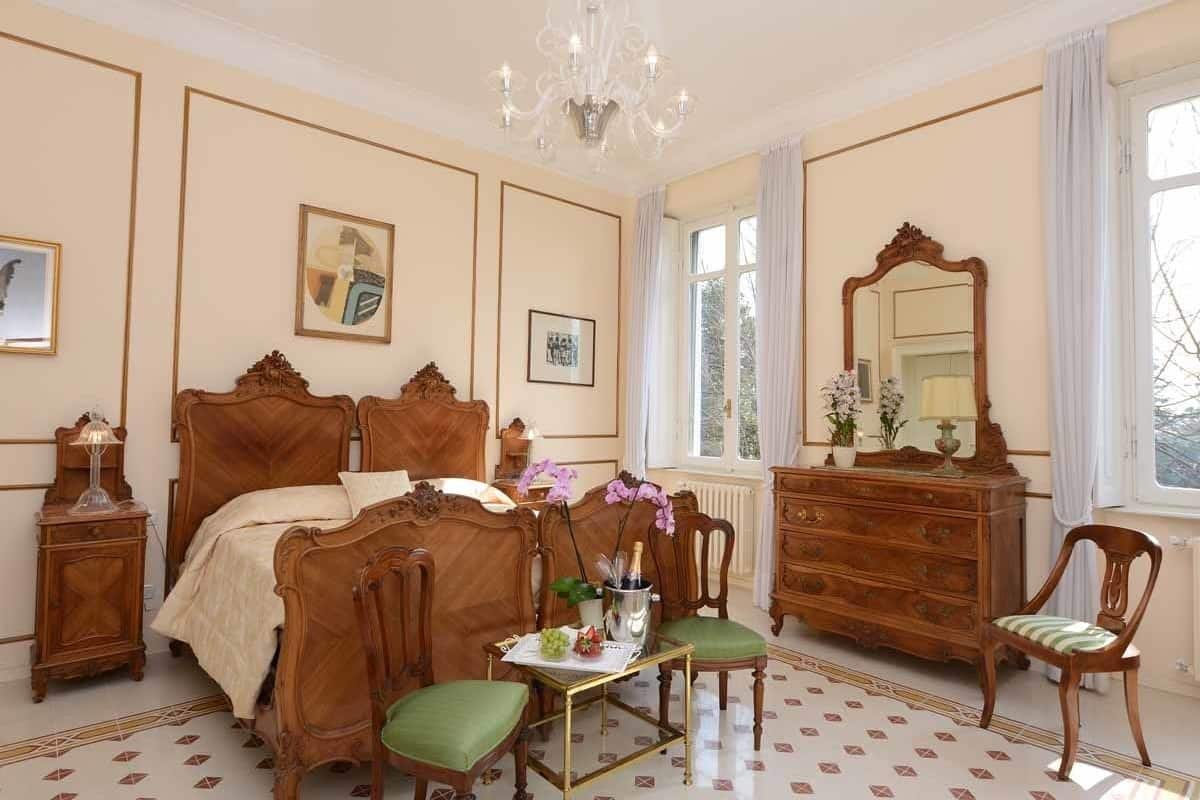 Ein klassisches Schlafzimmer mit einem hölzernen Bett, einem Schminktisch, einem Sessel und einer Kronleuchter.