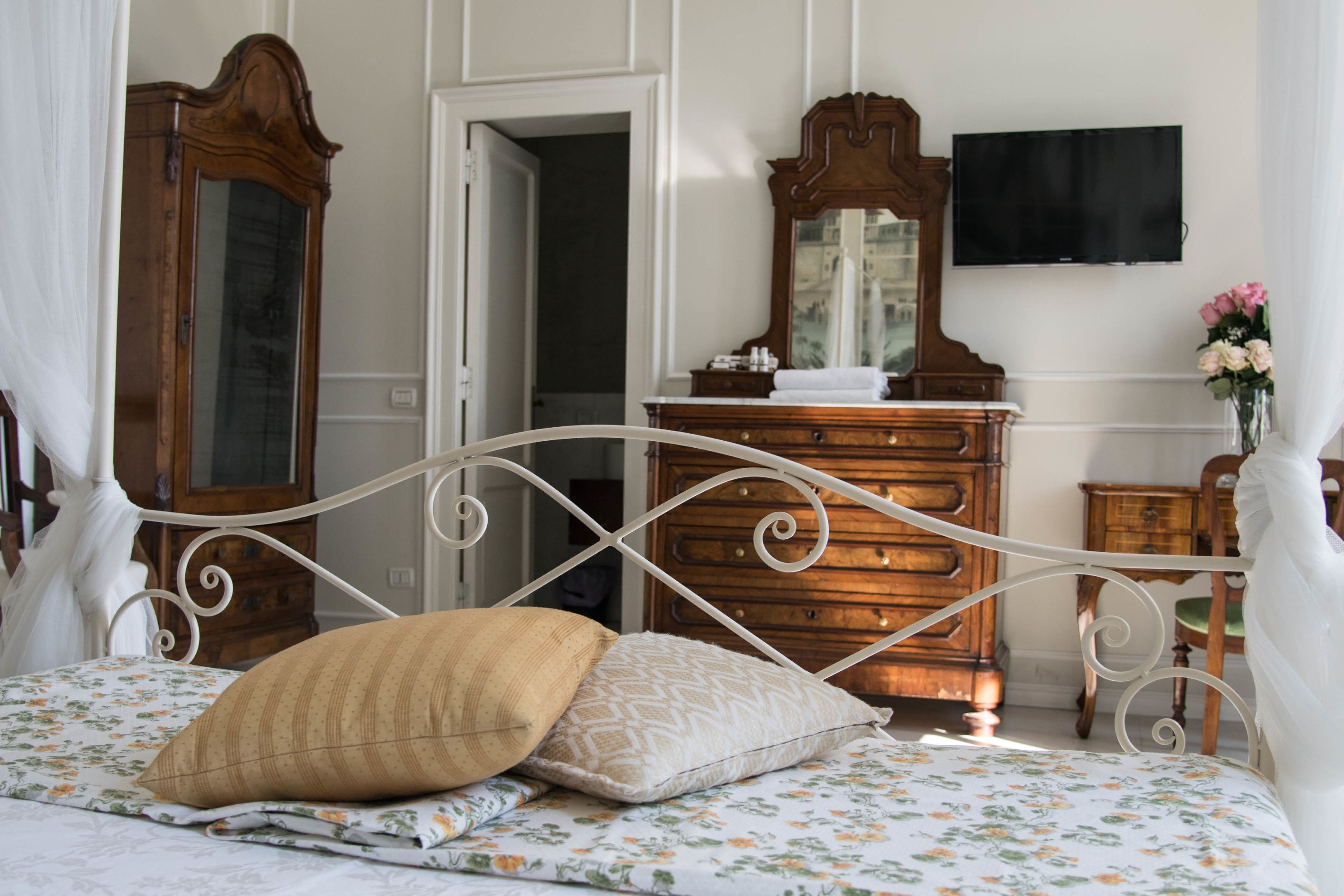 A neatly arranged bedroom with a bed, a dresser, a mirror, and a television.
