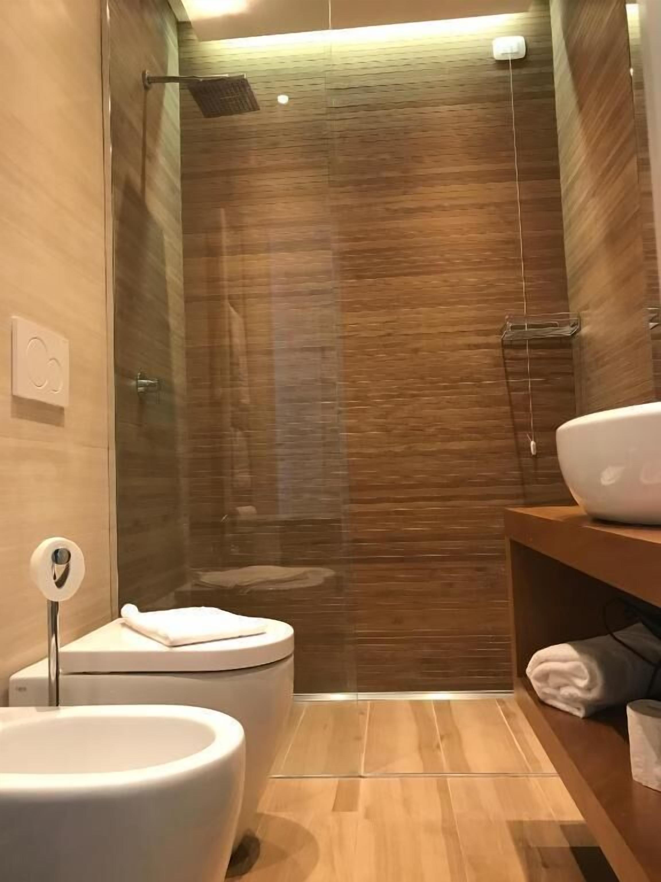 Een moderne badkamer met een glazen douchecabine, een wit toilet en een houten wastafelmeubel met een wastafel.