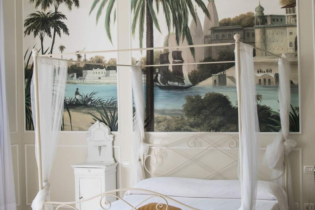 Ein Himmelbett mit Baldachin, einer Kristallleuchter und einem Wandgemälde mit Meeresblick.