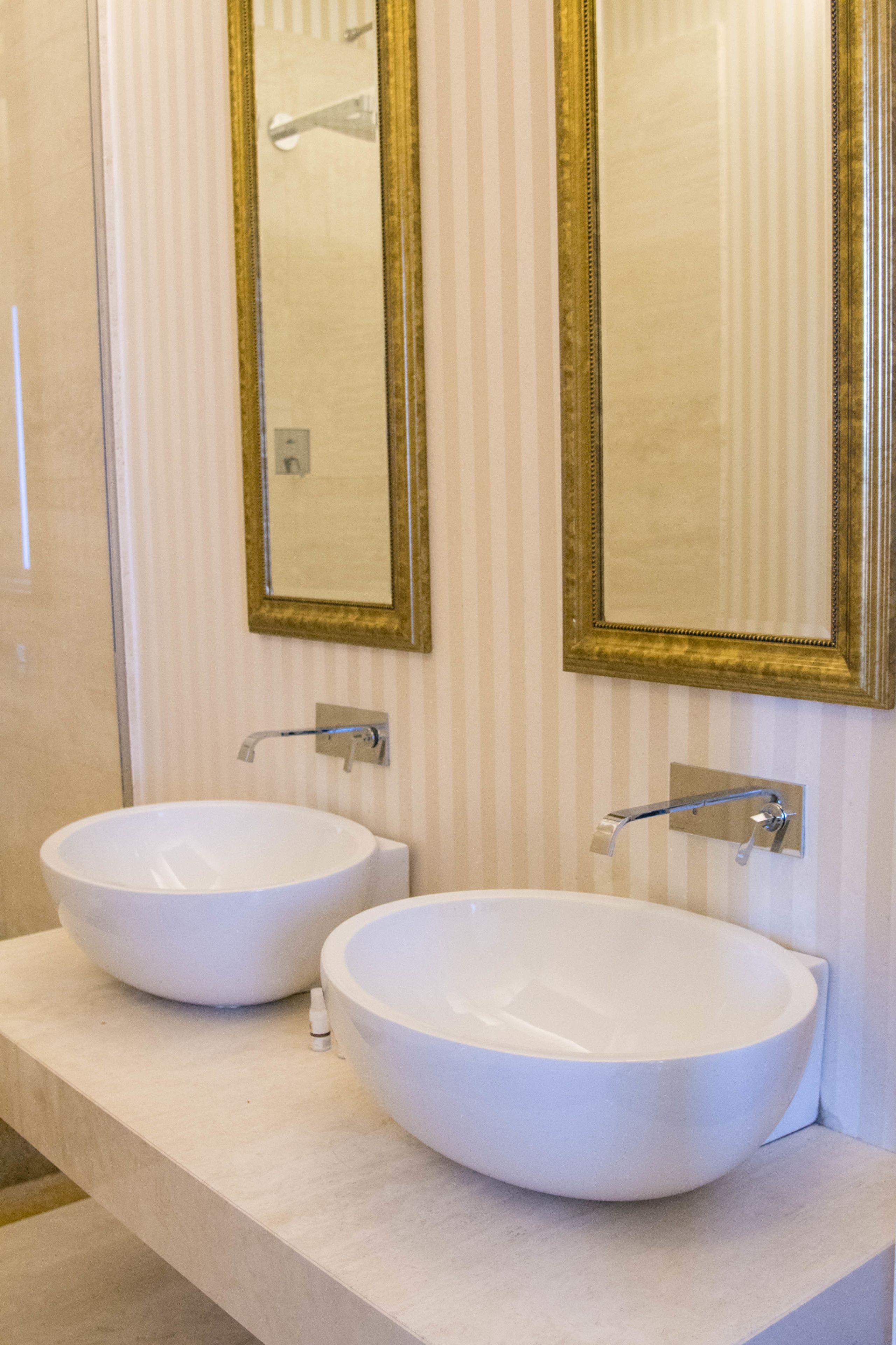 A bathroom with two white vessel sinks, a mirror with a gold frame, and a striped wall.