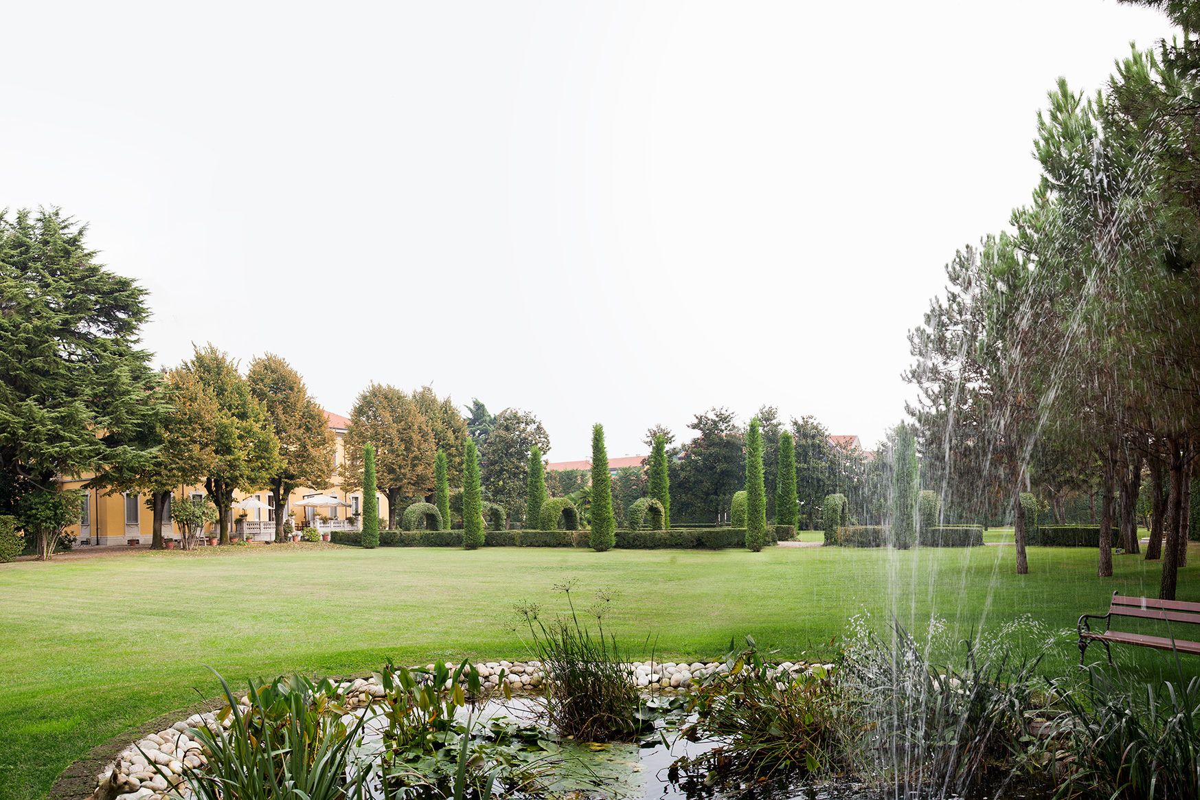 A well-maintained garden with a fountain, neatly trimmed hedges, and a variety of trees.