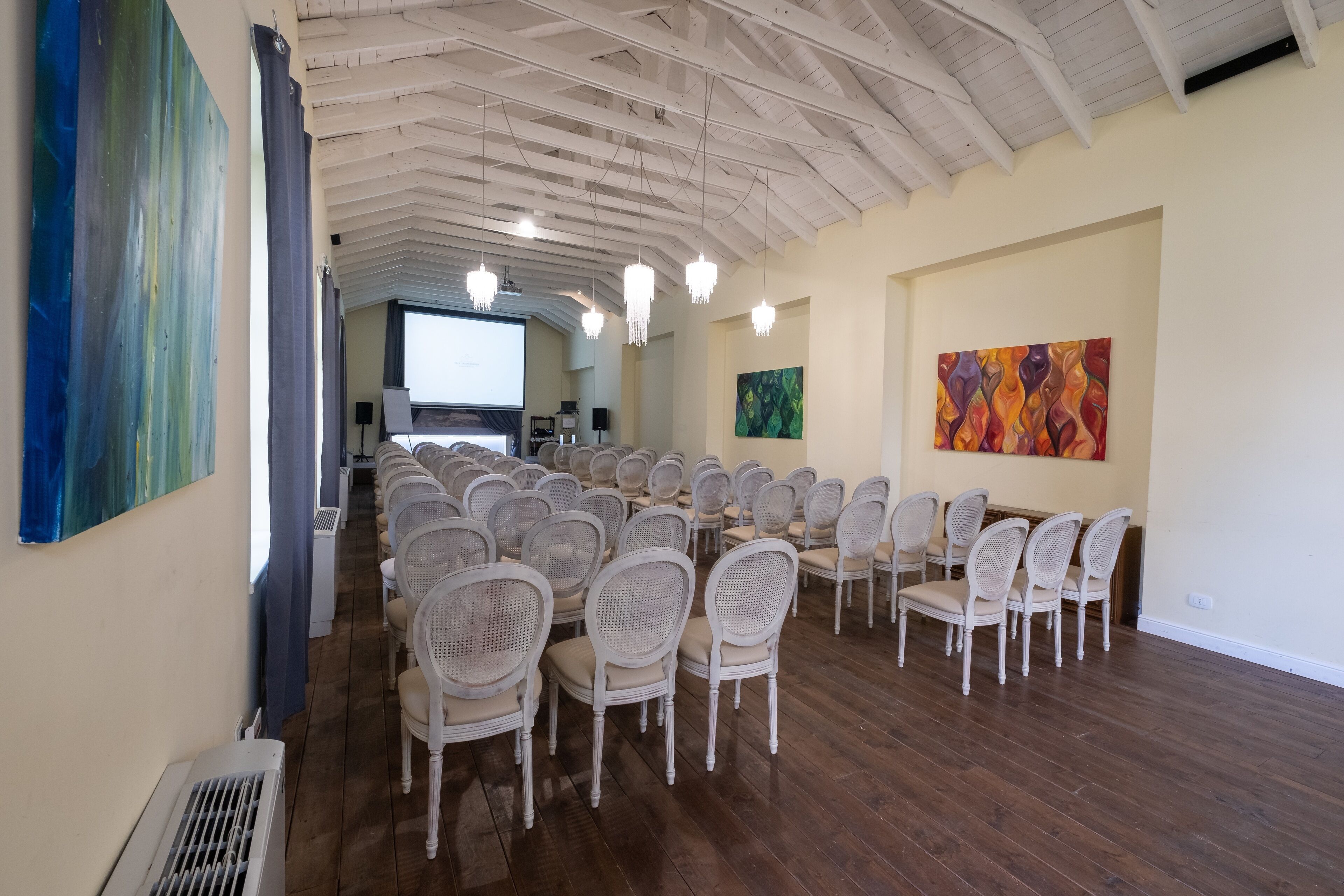 Een vergaderzaal met witte rotanstoelen en een projectiescherm.