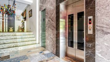 A modern lobby with a marble floor, a staircase with patterned tiles, and a glass elevator.