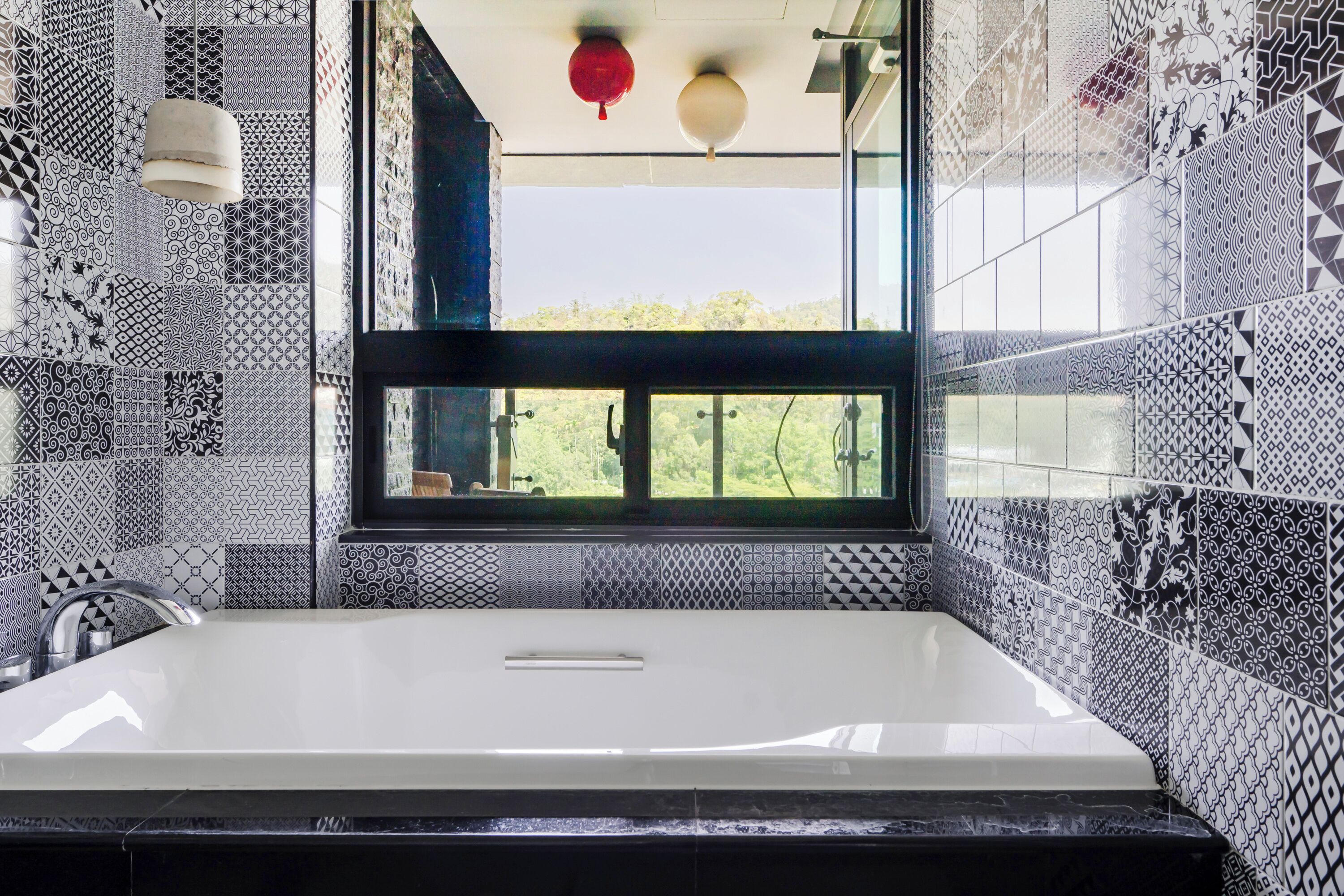 A bathroom with a large bathtub, patterned tiles, and a window with a view of greenery.
