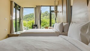 Ett hotellrum med två sängar, stora fönster och utsikt över grönområden.