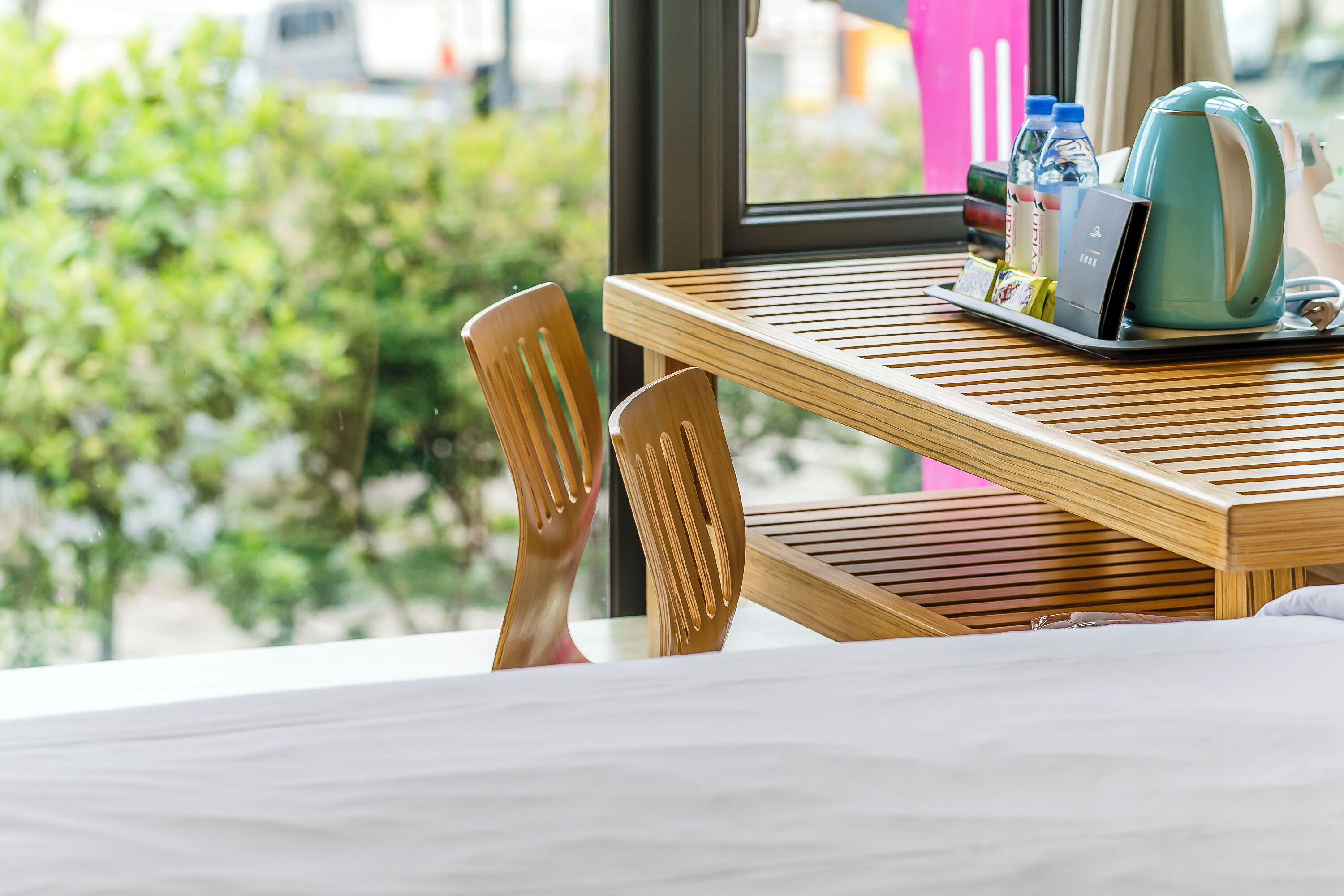 Une chambre d’hôtel avec une table en bois, un plateau contenant une bouilloire, des bouteilles et un téléphone portable.