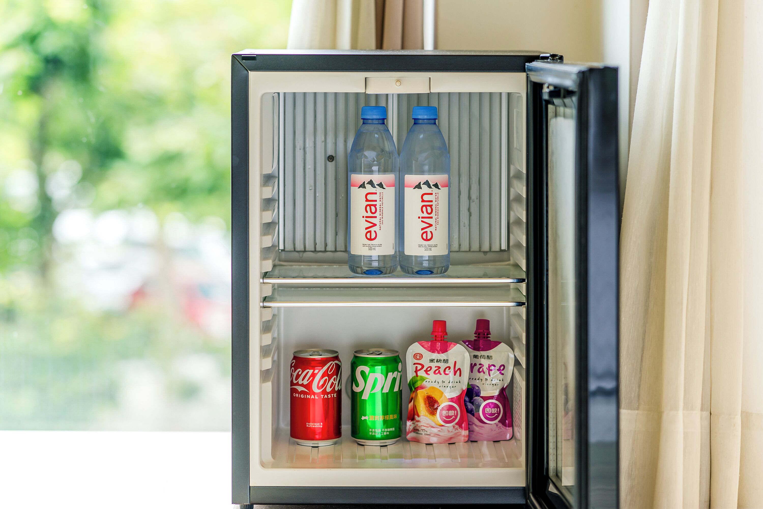 Un mini refrigerador con dos botellas de Evian y diversas bebidas, como Sprite, Coca-Cola, Peach y V8.