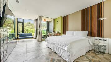 A modern hotel room with a large bed, a desk, and a balcony with a view of greenery.