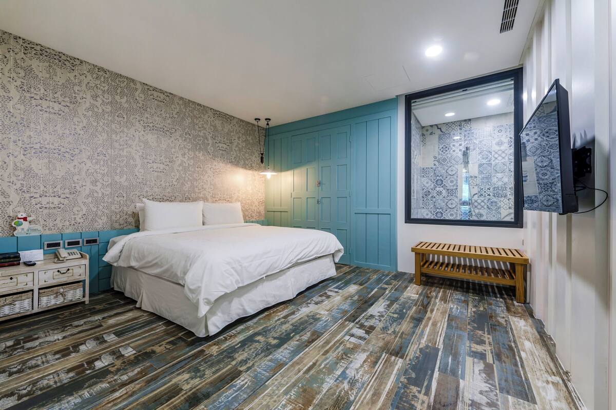 A bedroom with a bed, a wooden bench, a TV, and a patterned wall.