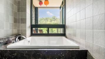 A modern bathroom with a large bathtub, a window with a view of greenery, and a black marble countertop.