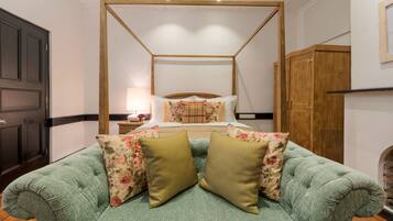 A four-poster bed with floral bedding, a green upholstered sofa with two cushions, and a wooden wardrobe.