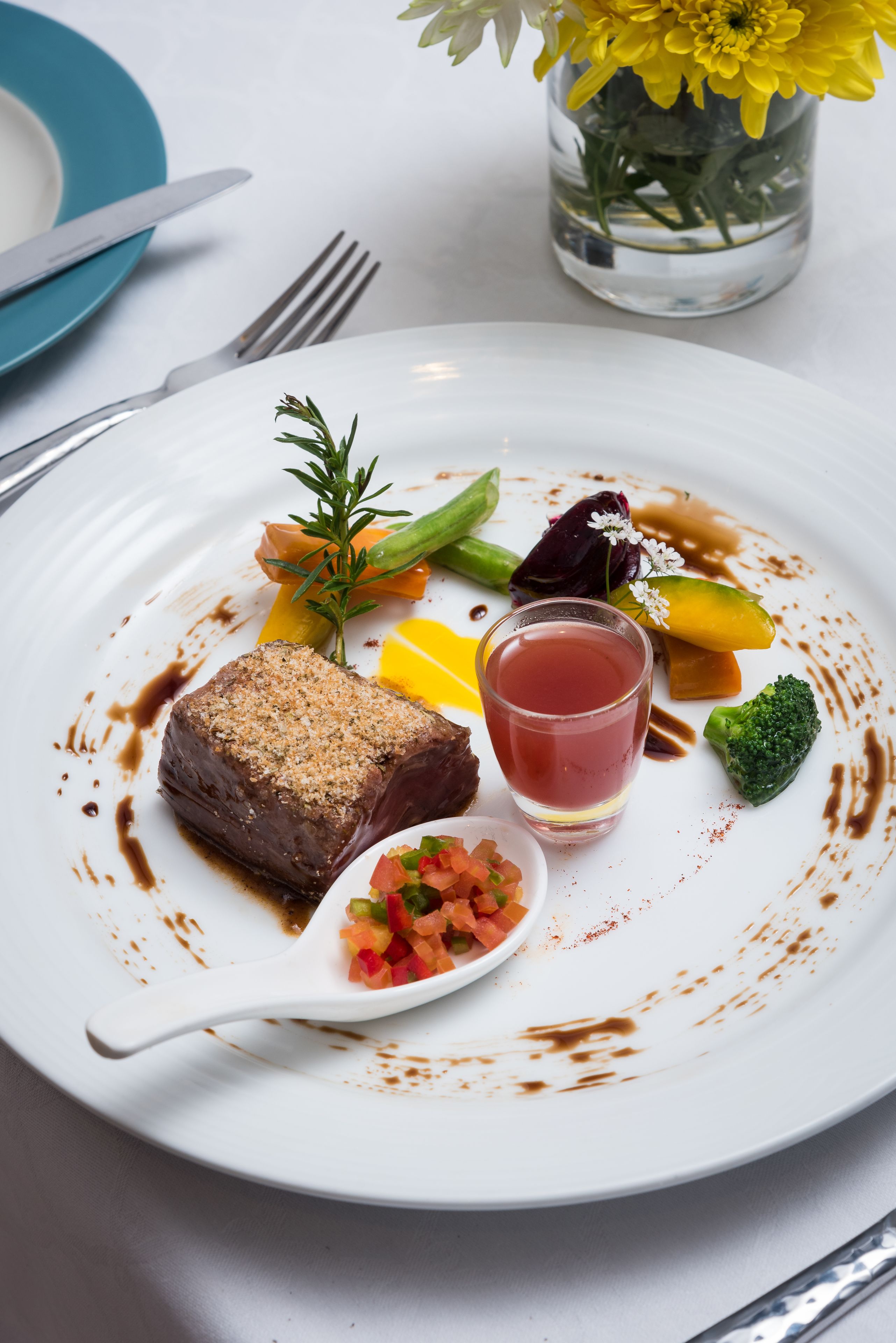 Une assiette blanche avec un steak, des légumes et un verre d’une boisson rouge.