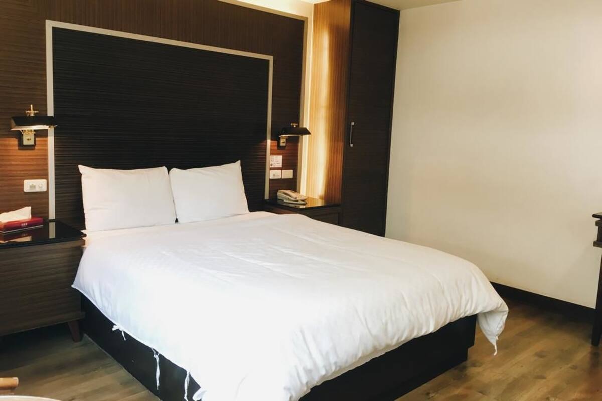 Une chambre d’hôtel moderne avec un grand lit, une tête de lit en bois, des lampes de chevet et une table de chevet avec un téléphone.