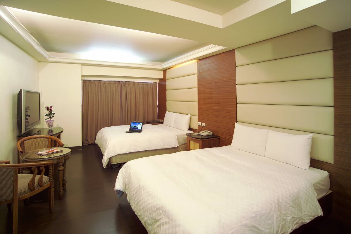 Une chambre d’hôtel avec deux lits, un bureau avec un ordinateur portable, une chaise et une télévision.