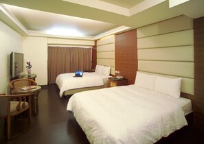 A hotel room with two beds, a desk with a laptop, a chair, and a television.