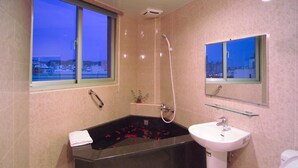 A modern bathroom with a black bathtub, a white sink, and a window with a view of buildings. - Hua Tai Hotel (Hsinchu)