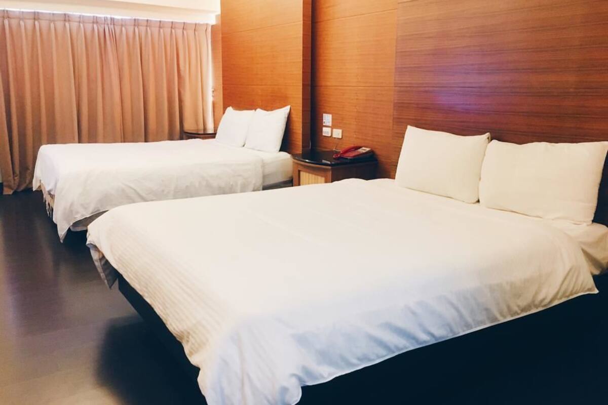 Une chambre d’hôtel avec deux lits, des lambris en bois sur les murs, une table de chevet avec un téléphone et un rideau à la fenêtre.