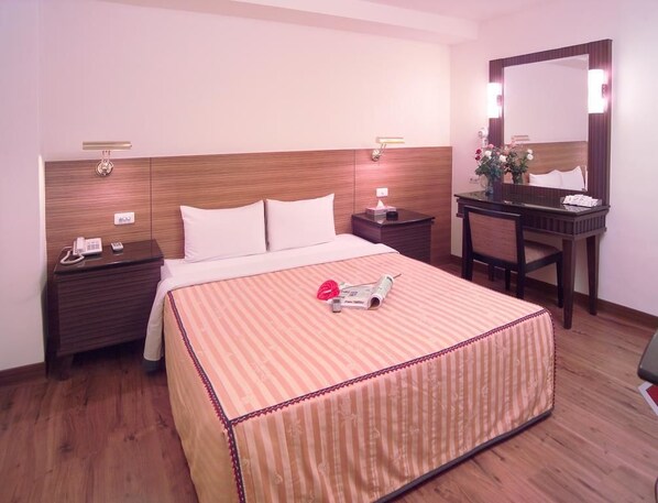 A hotel room with a wooden headboard, a bed with a striped bedspread, a bedside table with a phone and a lamp, a small desk with a mirror, and a chair. - Hua Tai Hotel (Hsinchu)