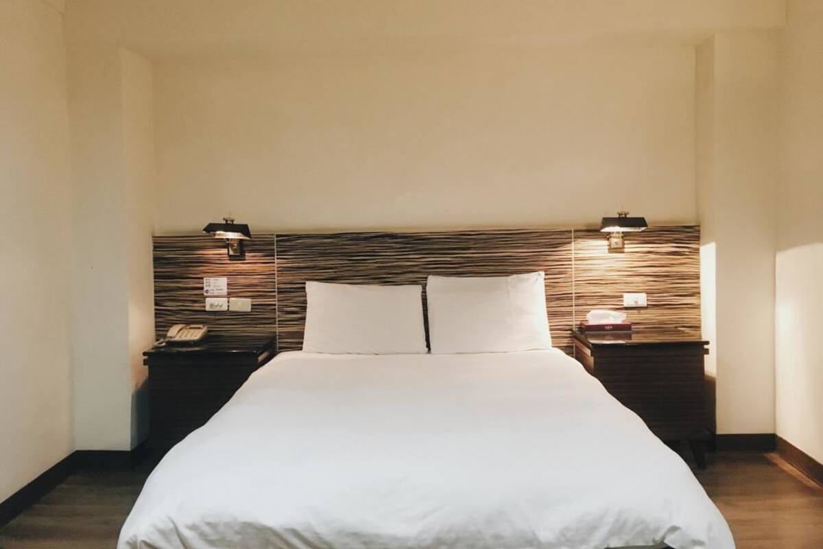 Une chambre d’hôtel avec un grand lit, deux tables de chevet et une tête de lit dotée d’un éclairage intégré.