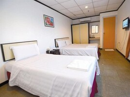 Quarto de hotel com duas camas, uma secretária pequena, uma televisão e banheiro com espelho.