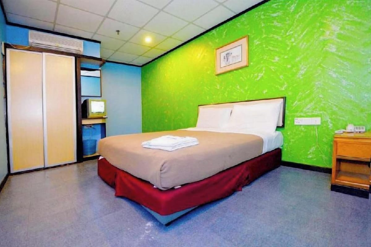 A hotel room with a bed, a desk, a chair, a wardrobe, and a green wall.