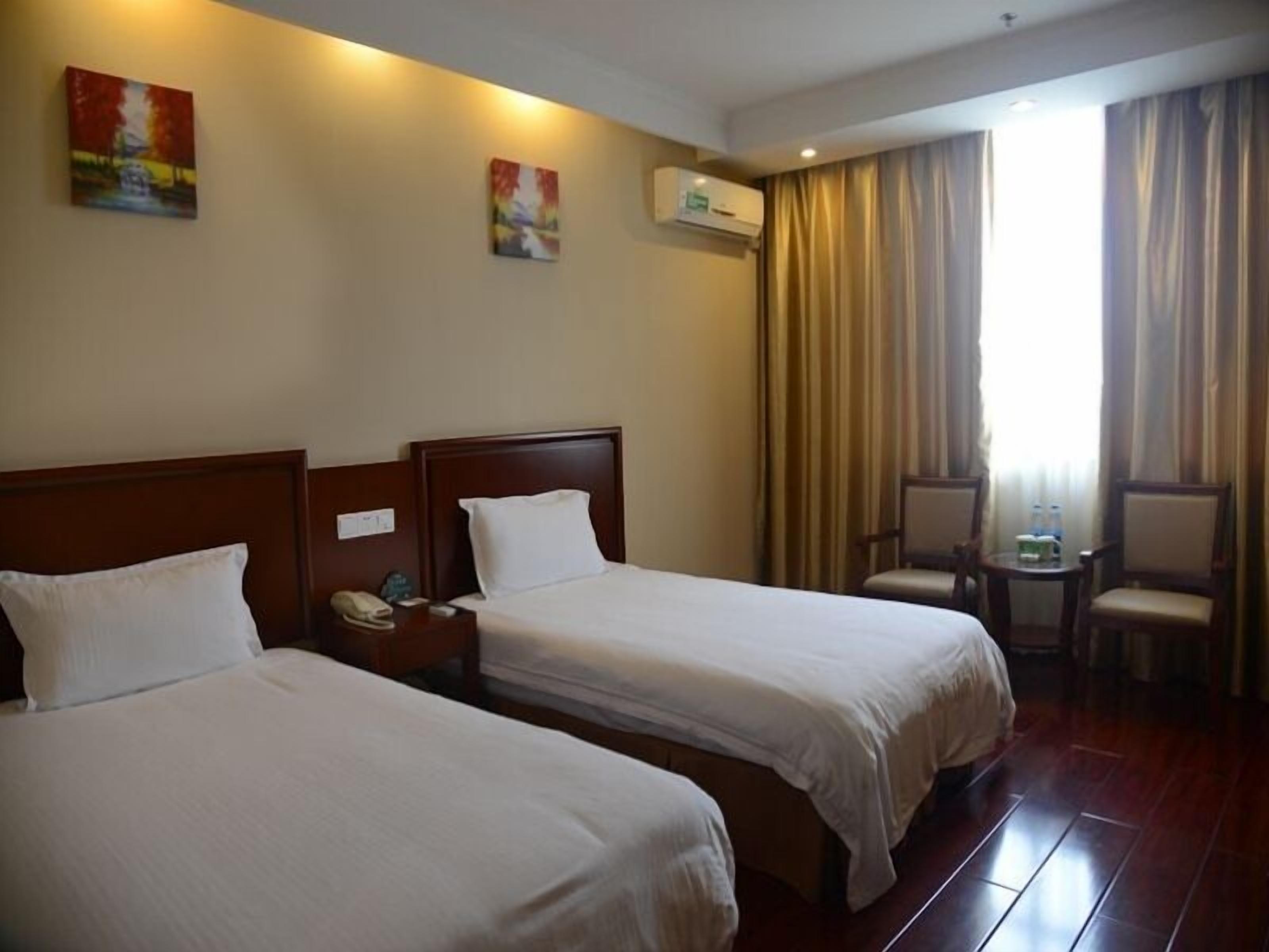 A hotel room with two beds, a nightstand with a phone, a chair, a small table with water bottles, and an air conditioning unit on the wall.