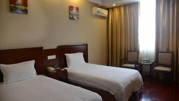 A hotel room with two beds, a nightstand with a phone, a chair, a small table with water bottles, and an air conditioning unit on the wall.