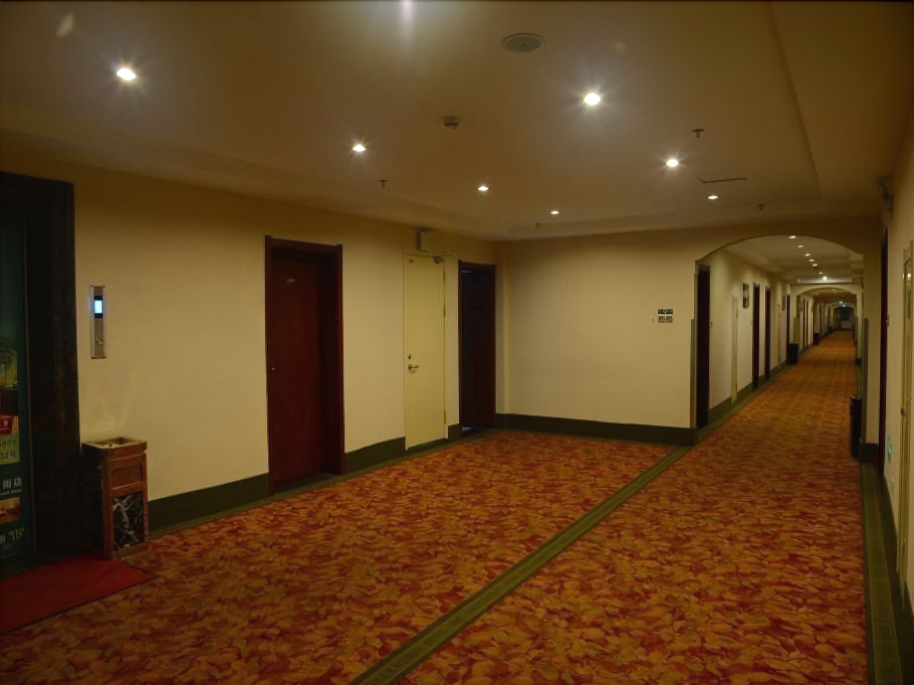 A hotel corridor with carpeted floors, doors, and a vending machine.