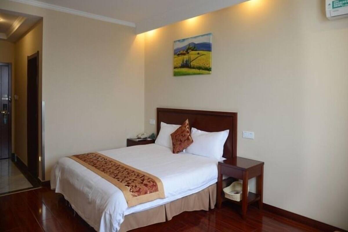 Een hotelkamer met een groot bed, een nachtkastje, een bijzettafeltje en een schilderij aan de muur.