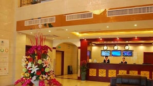 A hotel lobby with a reception desk, two monitors, a receptionist, a floral arrangement, and a seating area. - GreenTree Inn Huangshan Tunxi Old Street Hotel (Huangshan)