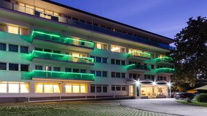 Um hotel com vários andares, varandas, entrada bem iluminada e um caminho de acesso pavimentado.
