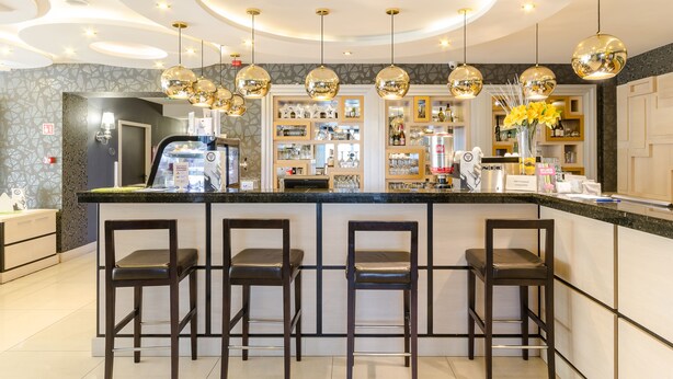 Uma área de bar com design moderno, com um balcão central, banquetas e iluminação decorativa.