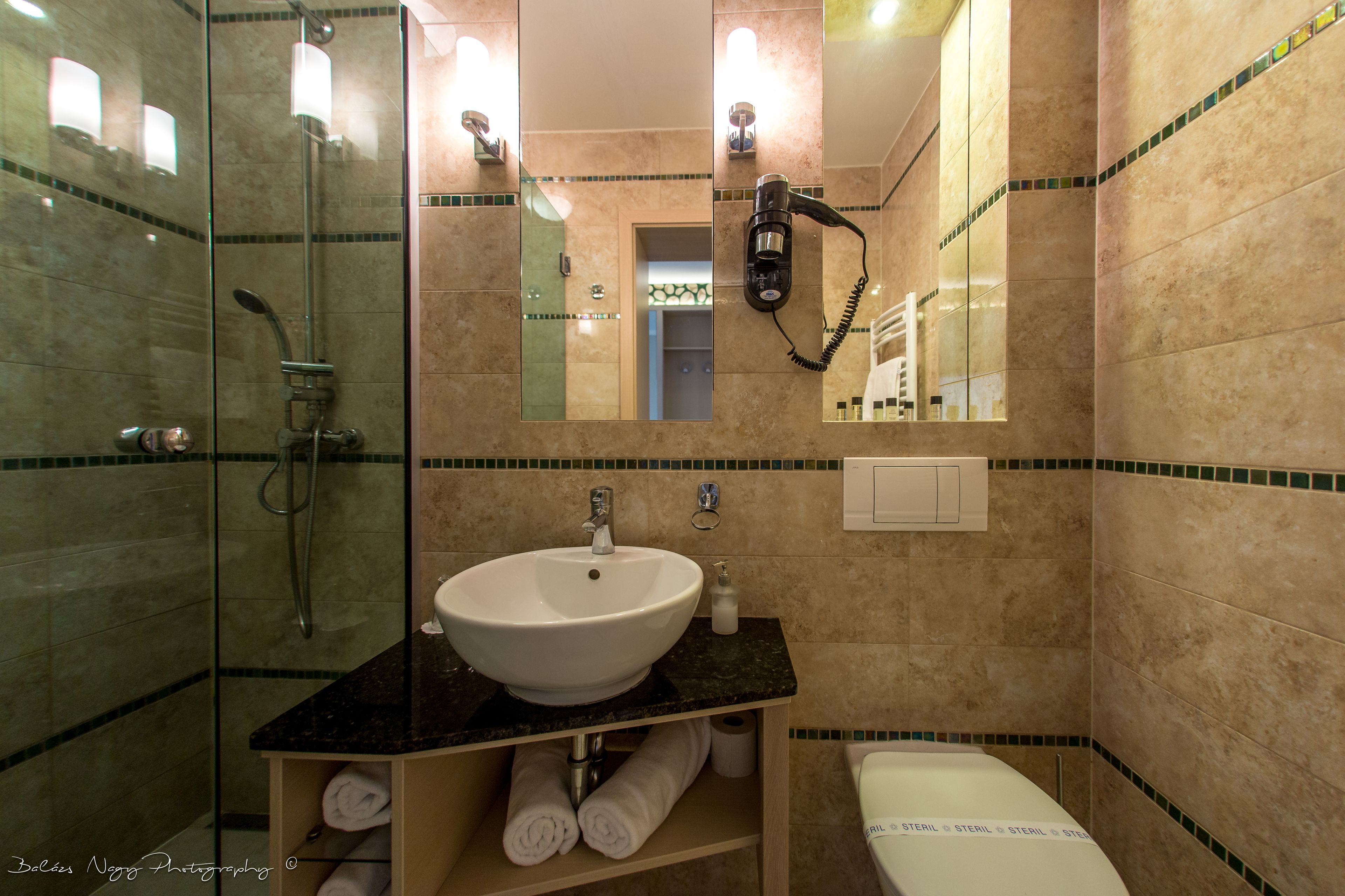 A bathroom with a glass-enclosed shower, a white sink with a black countertop, and a mirror above the sink.