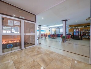 A spacious lobby with a restaurant sign, a vending machine, and a seating area with tables and chairs.
