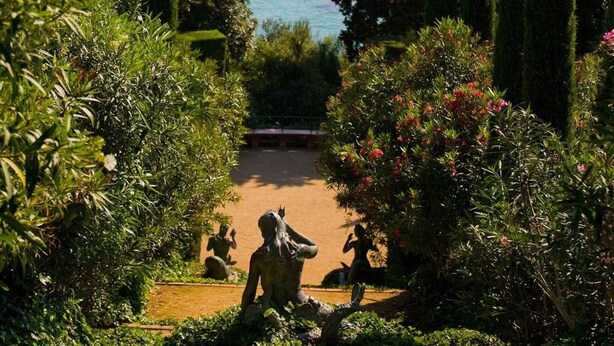 A garden with statues, a bench, and a view of the sea. - Golden Sand (Lloret de Mar)
