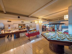 A buffet area with multiple food stations, a central serving table, and a kitchen area in the background. - Golden Sand (Lloret de Mar)