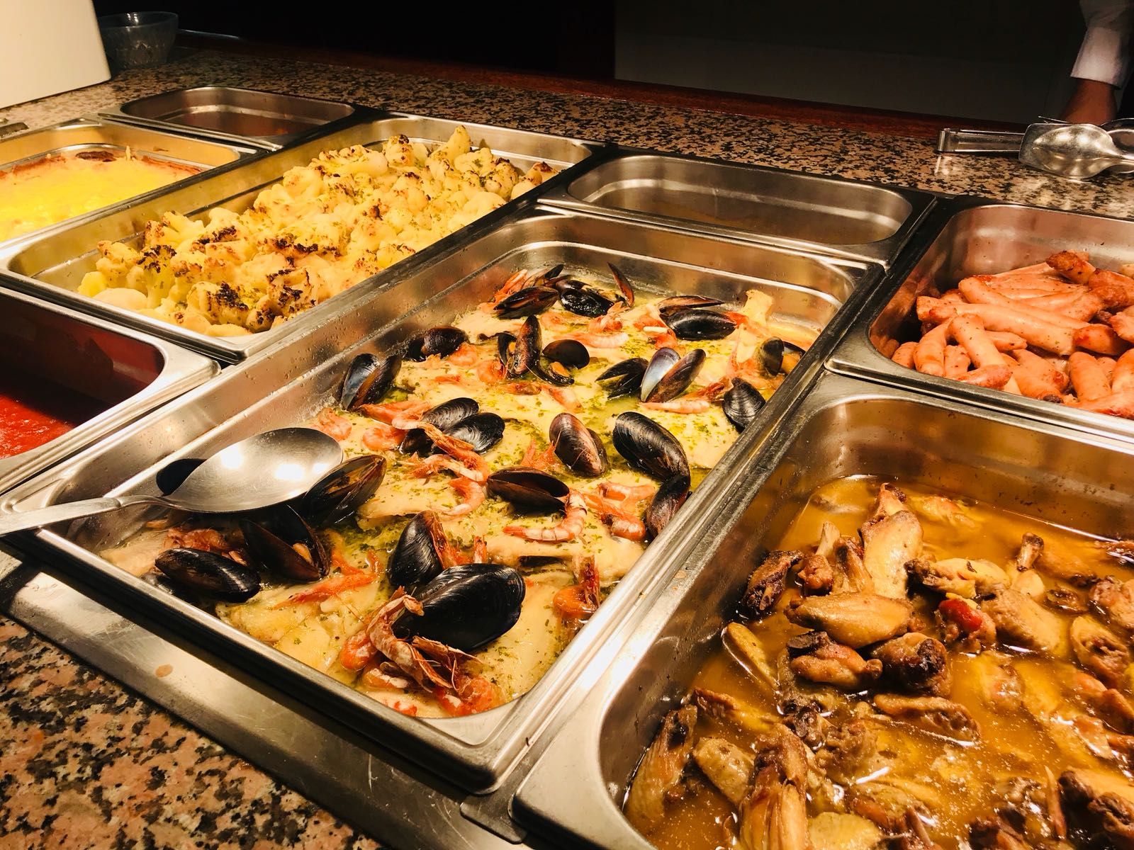 Un buffet proposant une variété de fruits de mer, notamment des moules, des crevettes et des ailes de poulet.