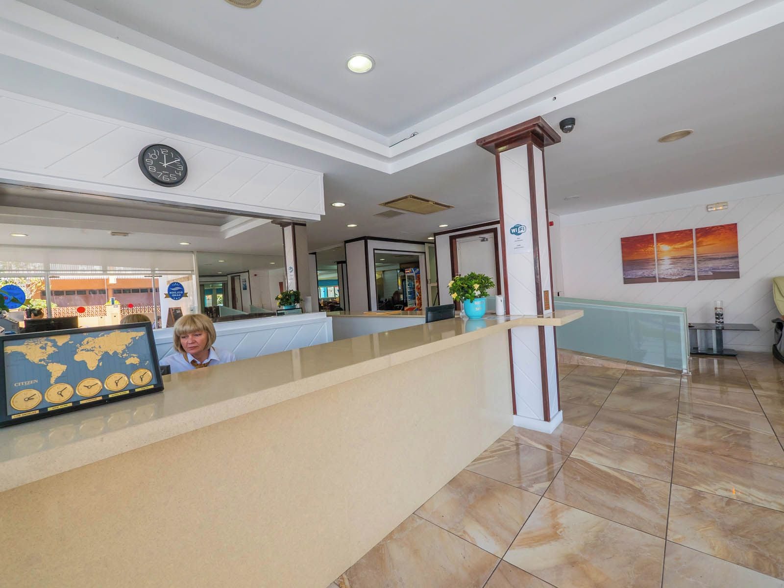 A hotel reception area with a reception desk, a world map display, a clock, and a Wi-Fi sign.
