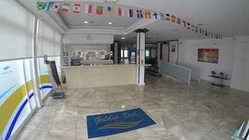Um hall de hotel com balcão de recepção, tapete de entrada e parede decorada com bandeiras de diversos países.
