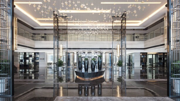 Een moderne lobby met een centraal gelegen waterpartij, glazen balustrades en een plafond met hangende bolvormige lampen.