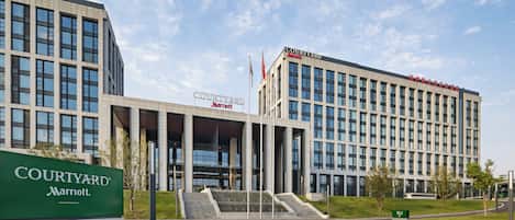 Un hotel Courtyard Marriott con un diseño arquitectónico moderno, que cuenta con una entrada destacada con escalones e izado de bandera.