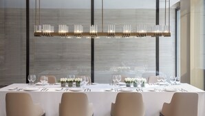 Een eetruimte met een lange tafel gedekt voor vier personen, met een moderne kroonluchter, een wit tafelkleed en stoelen.