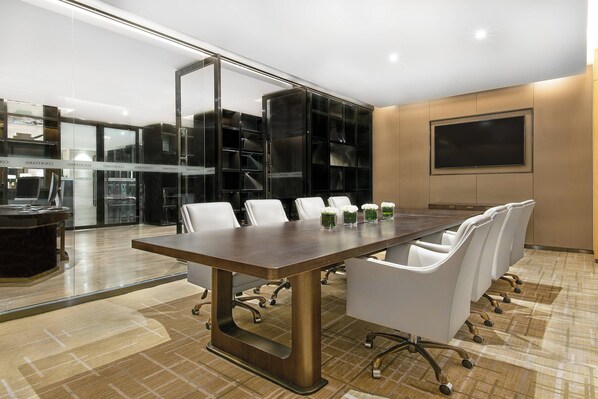 A modern conference room with a large table, white chairs, and a glass partition.