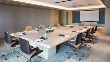 A conference room with a long table, chairs, a projector screen, and a carpeted floor.